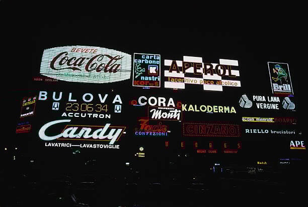gettyimages-2236253049-612x612 - A group of neon advertisements (including 'Cola-Cola', 'Carta Carbone Nastri Kores', 'Aperol', 'Brill', Bulova', 'Koloderma', wool (Pura Lana Vergine), 'Candy', and 'Cinzano') illuminated at night in Milan, Lombardy, Italy, 1960. (Photo by Alon Reininger/Archive Photos/Getty Images)