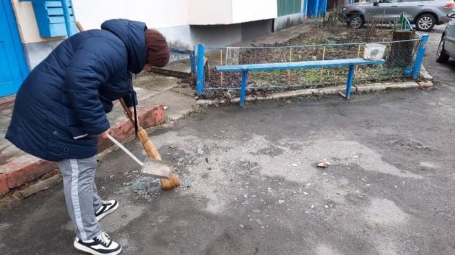 Жителька Красилова Марина замітає скло біля під&#039;їзду свого будинку, яке вилетіло через вибухову хвилю. 15 лютого 2024 рік. 